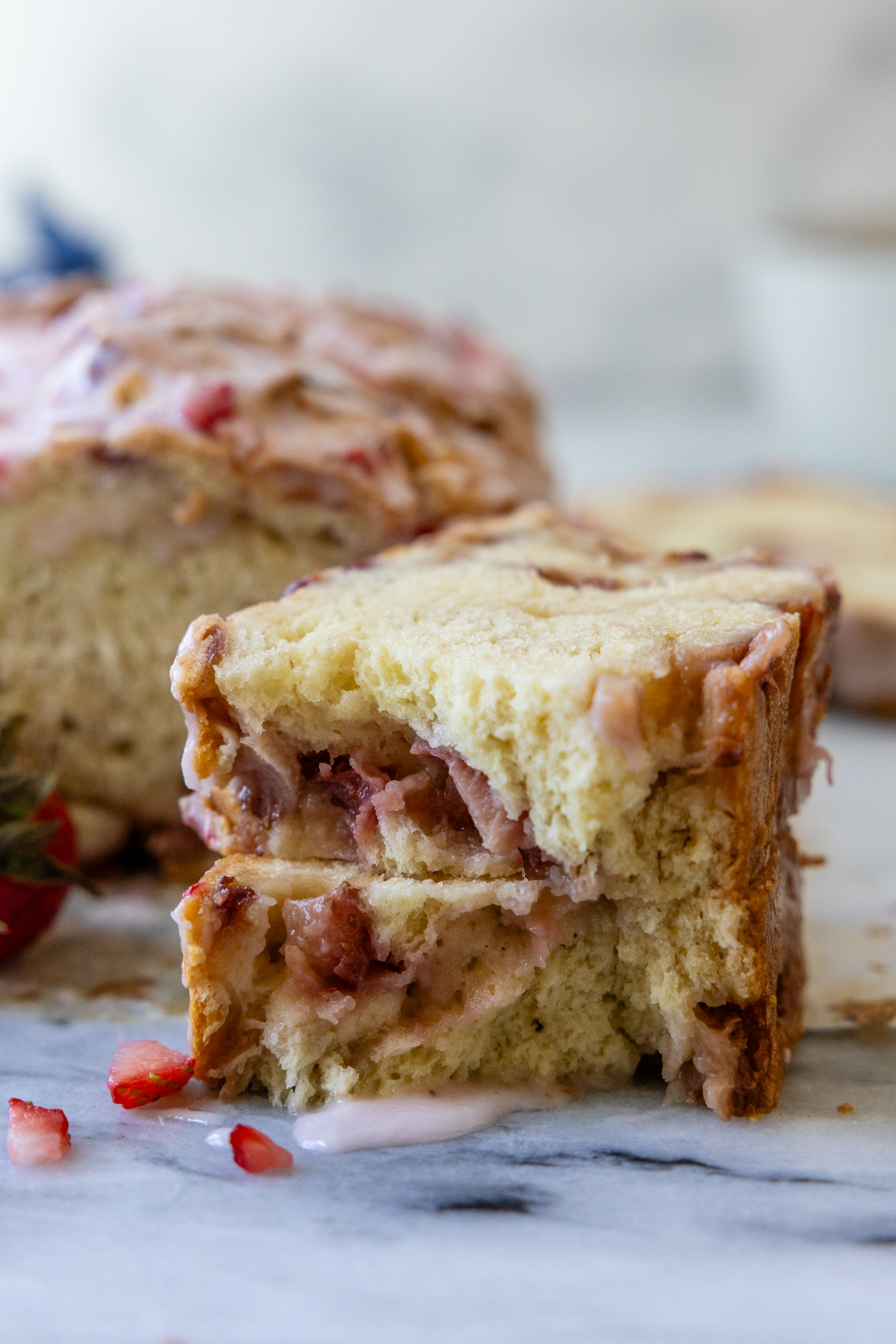 strawberry bread slice broken in half on a marble surface with glaze dripping down.