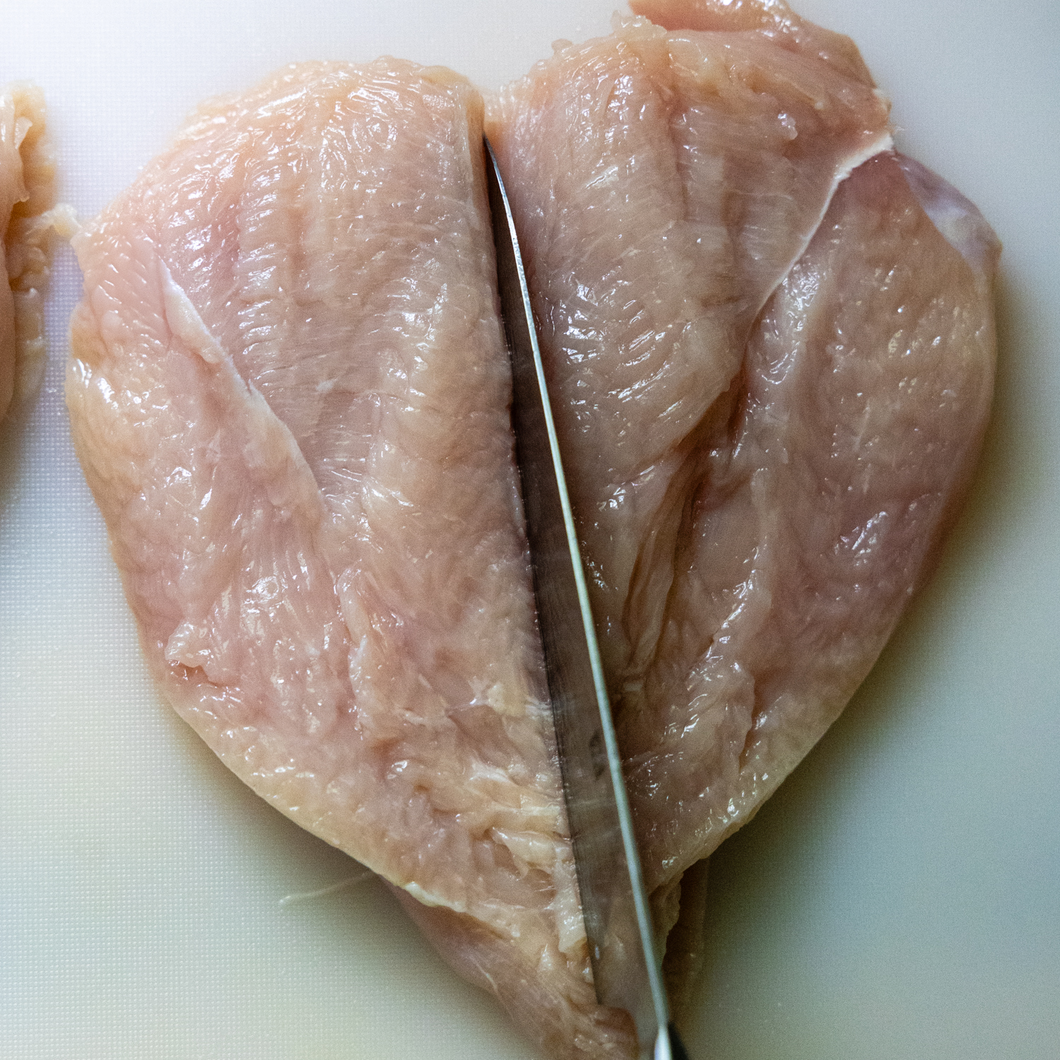 Raw chicken cutlet being cut in half.