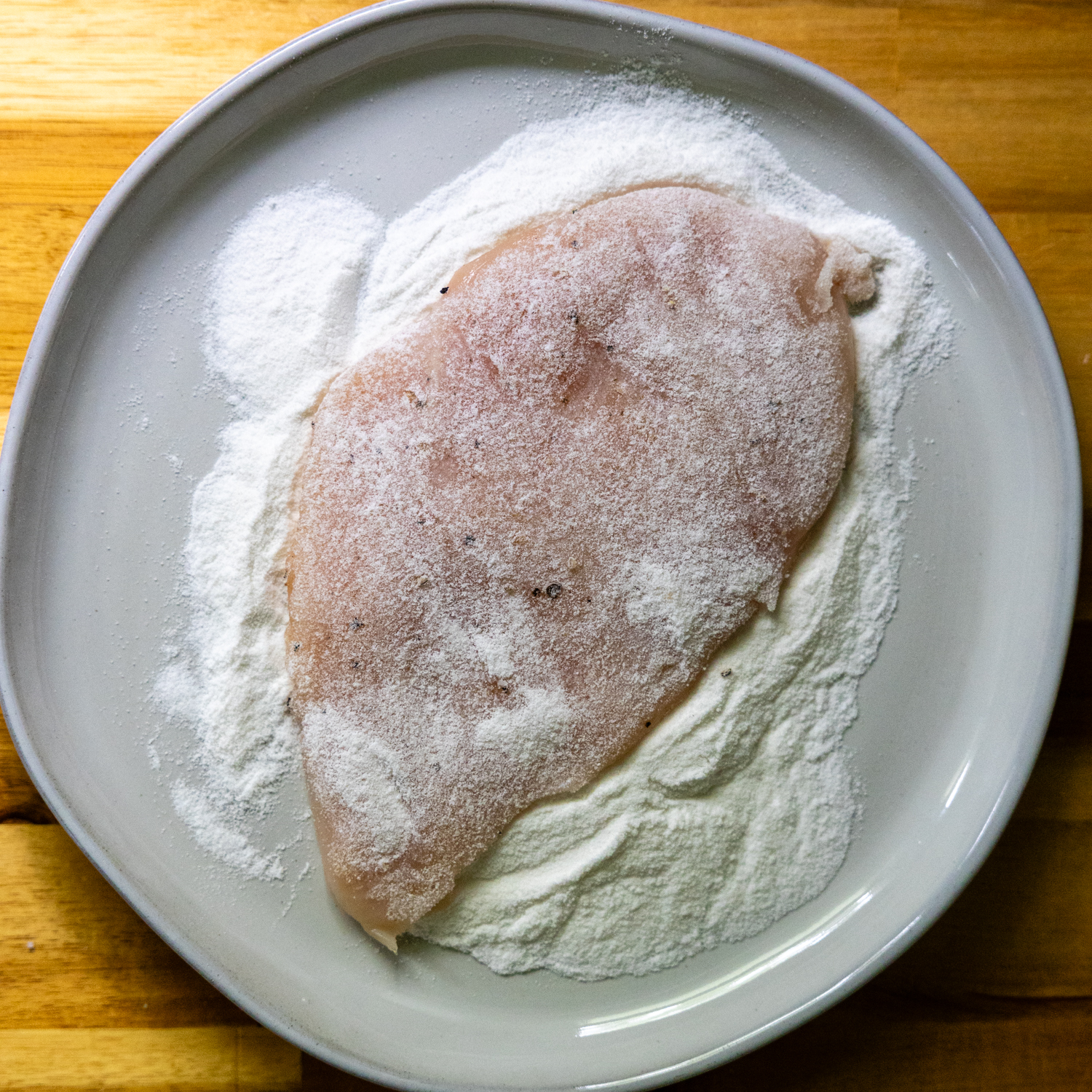 Chicken cutlet being dredged in rice flour.