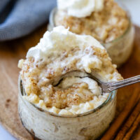 a spoon going into a small glass bowl of rice pudding with whipped cream on top.