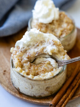 a spoon going into a small glass bowl of rice pudding with whipped cream on top.
