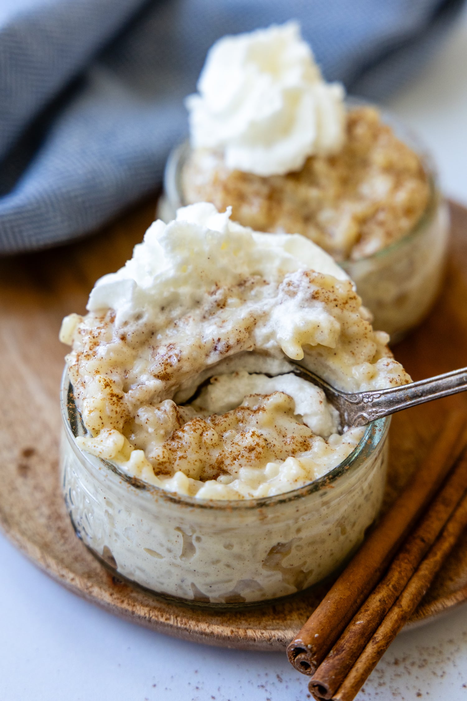 a spoon going into a small glass bowl of rice pudding with whipped cream on top.