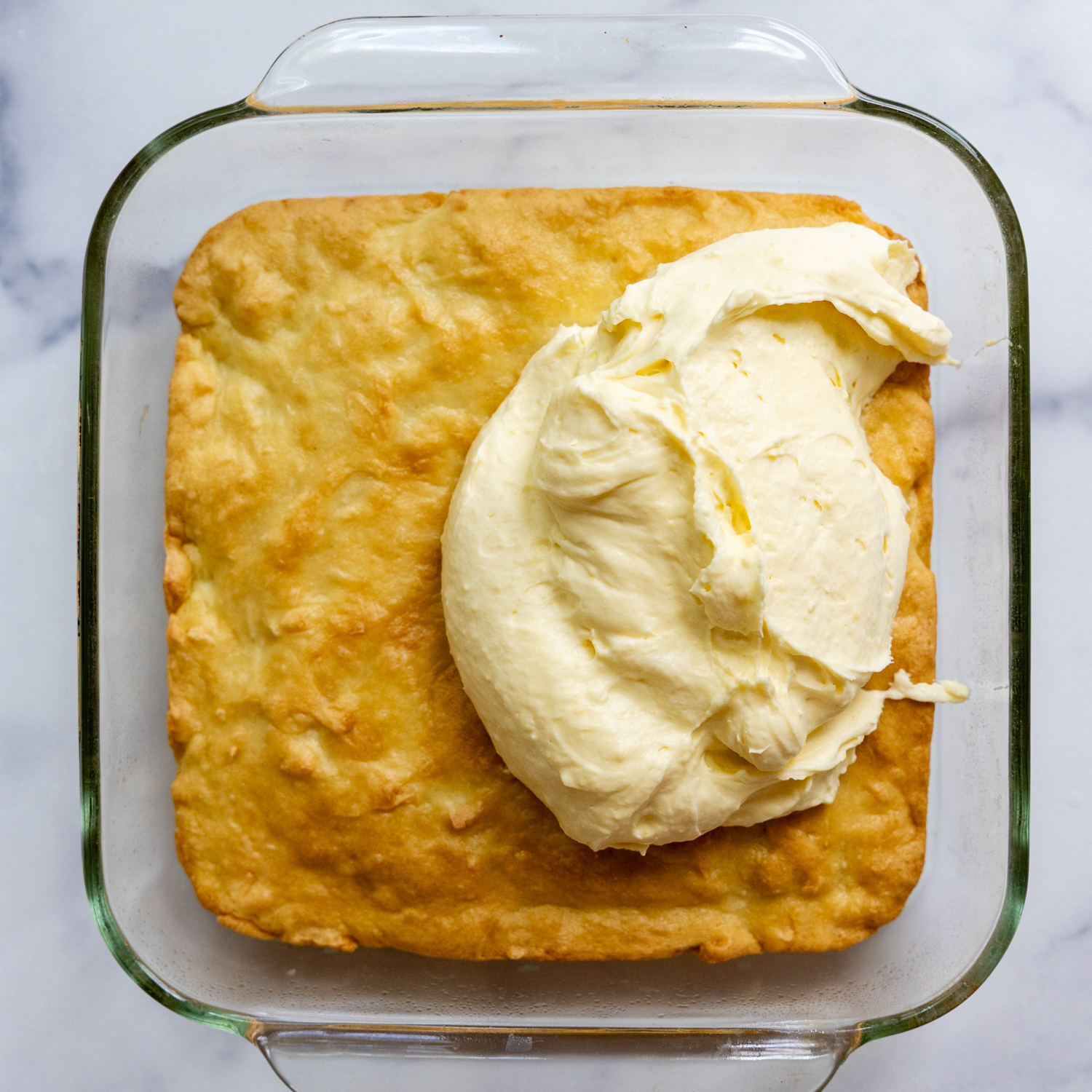 Cake in a glass baking dish with glob of frosting on top.