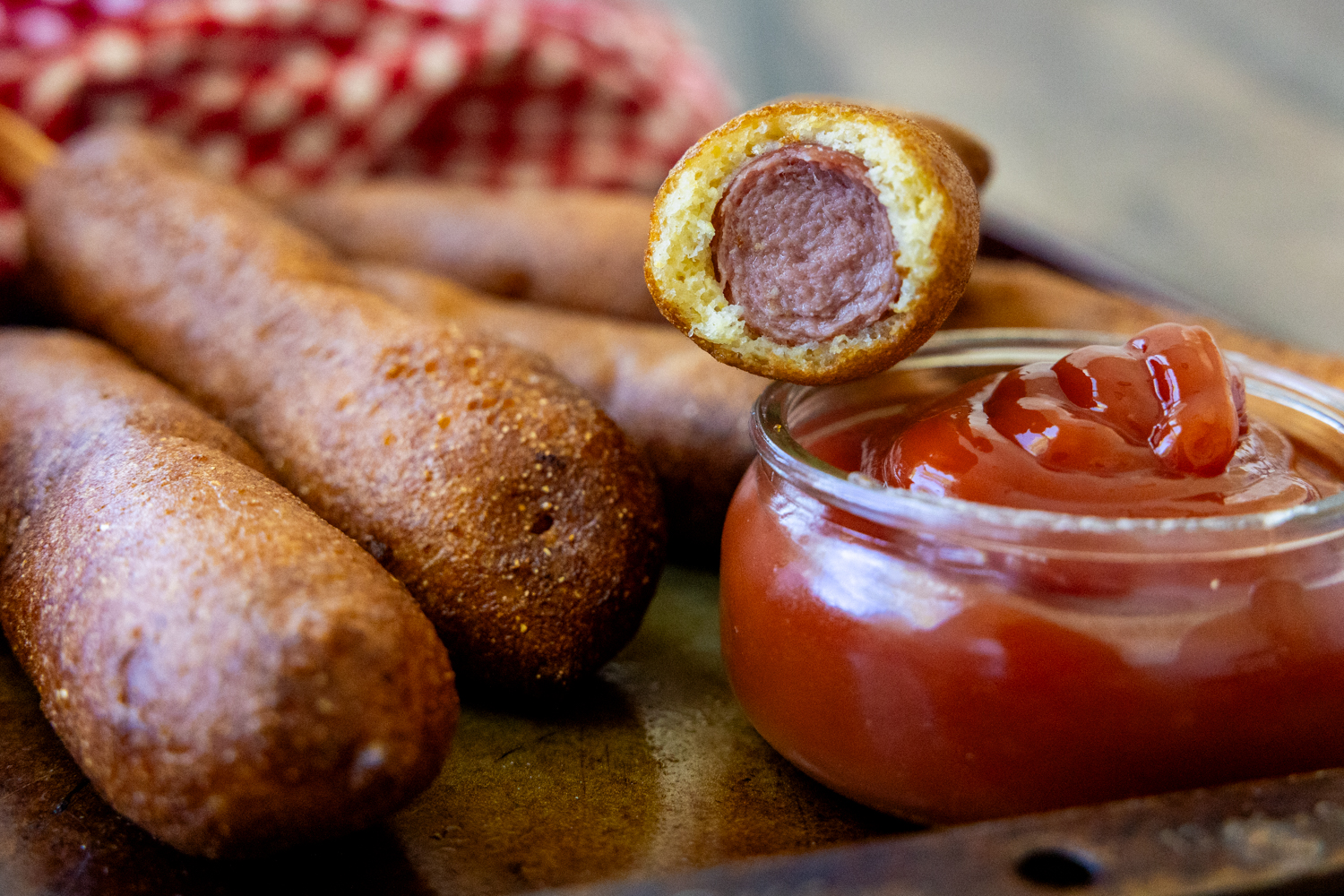Gluten free corn dogs with one of the corn dogs showing the inside while sitting on dipping sauce.