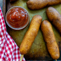 Gluten free corn dogs on a pan with a side of dipping sauce.