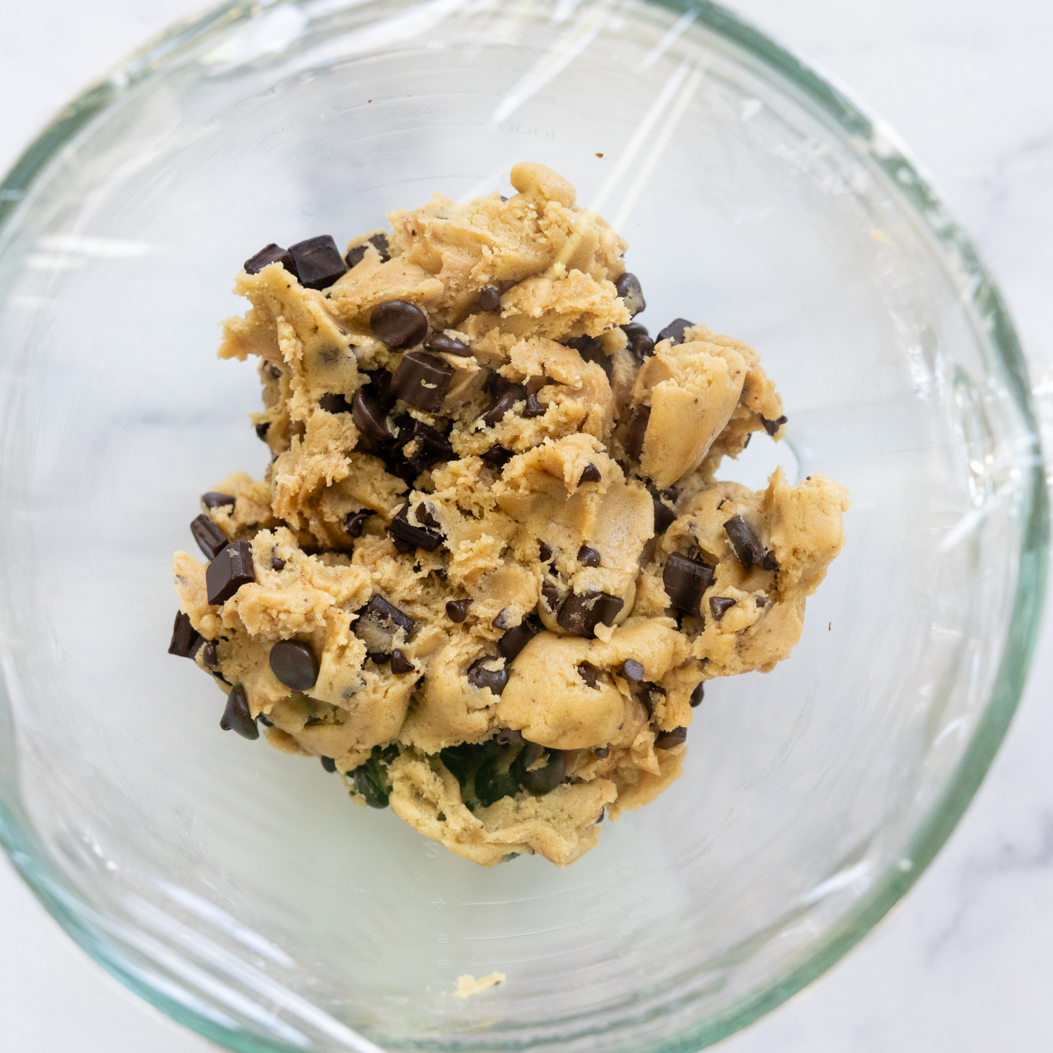 Chocolate chips added to cookie dough in a glass bowl.