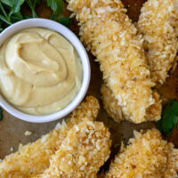 Gluten Free Chicken Fingers on a serving plate laying next to a bowl of sauce.