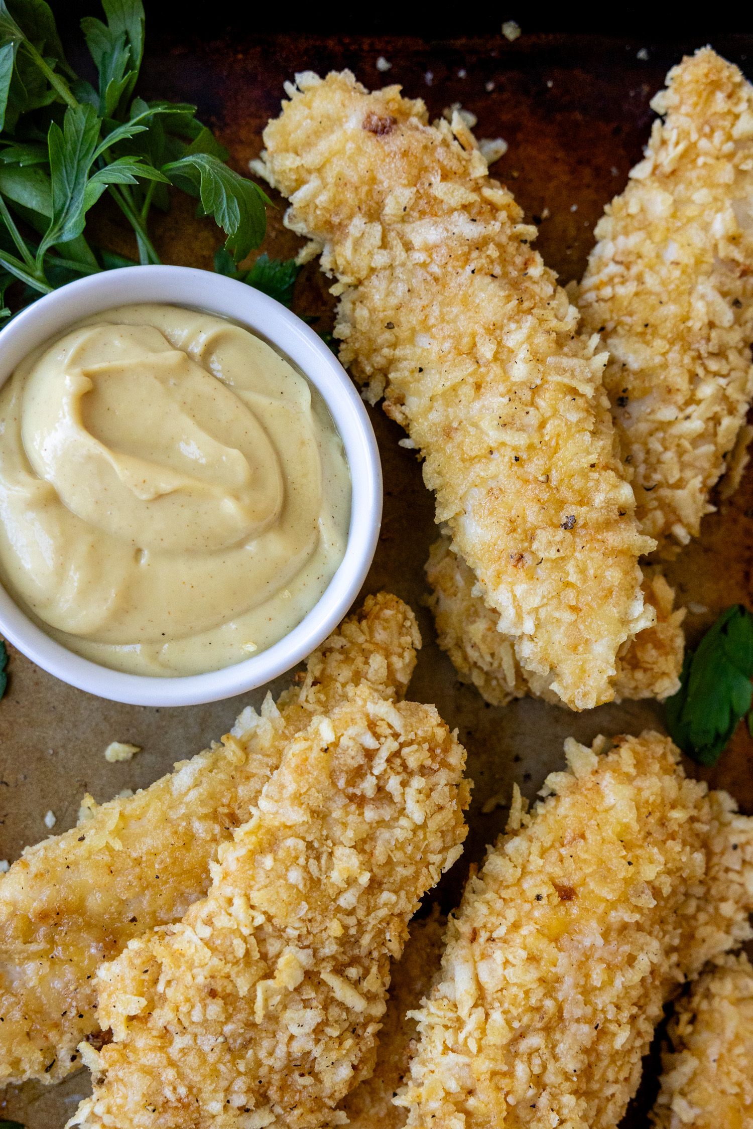 Chicken fingers on a serving plate laying next to a bowl of sauce.