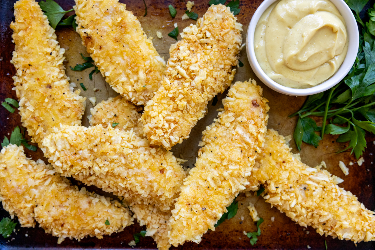 Cooked chicken fingers on a pan with dipping sauce.