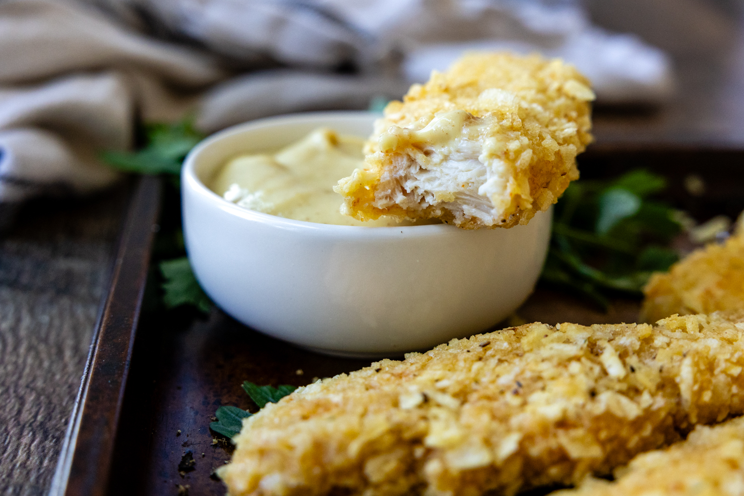 Chicken finger cut in half laying on a dish of sauce.