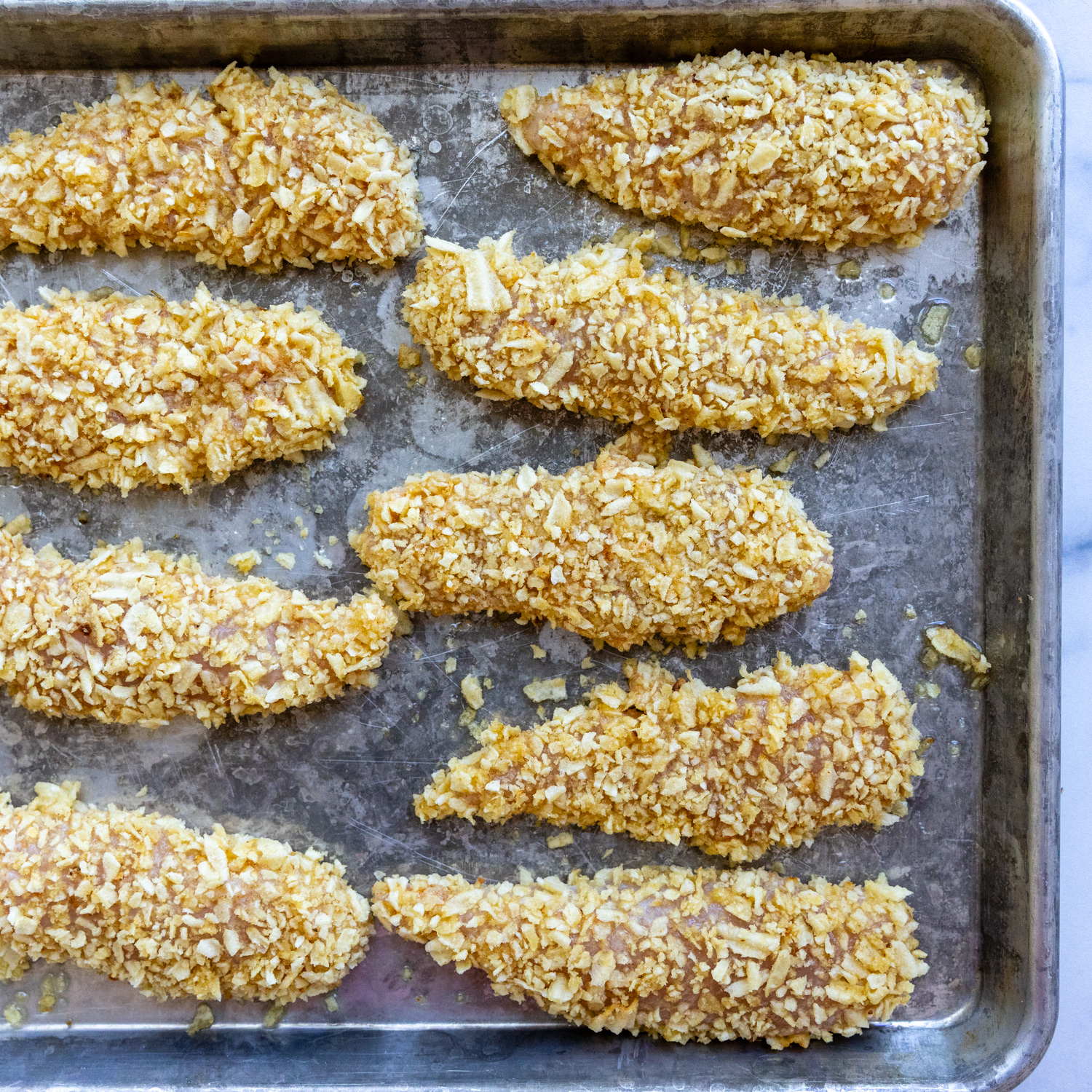 Coated chicken fingers on a pan.