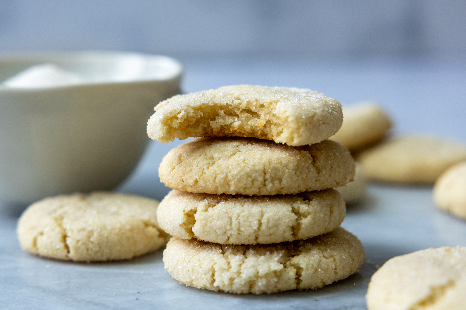 Four cookies stack on top of one another with a white bowl in background.