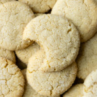 A pile of almond flour sugar cookies with the one on top having had a bite taken from it.