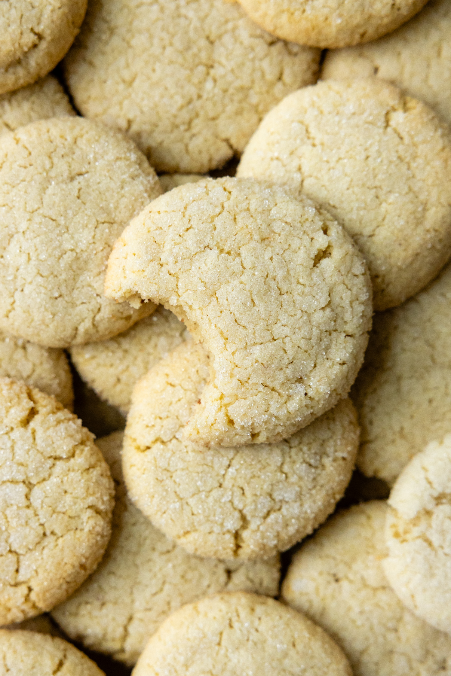A pile of almond flour sugar cookies with the one on top having had a bite taken from it.